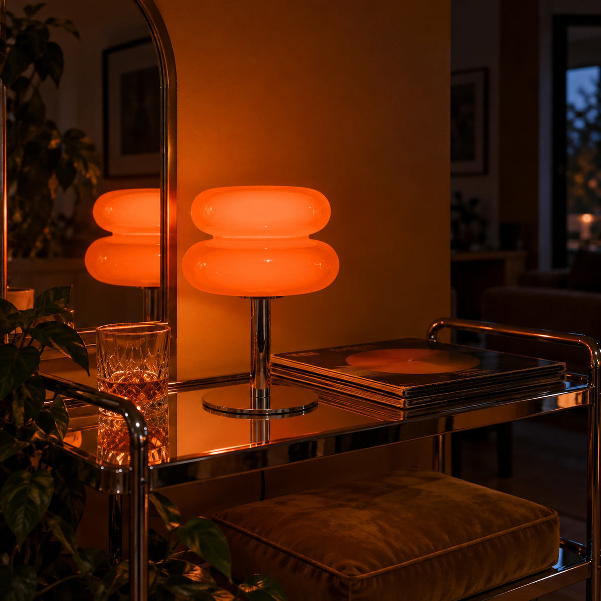 Aprica Table Lamp lit on a chrome bar cart beside an arched mirror