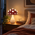 Large red mushroom lamp with white spots glowing as the only light beside a bed at night