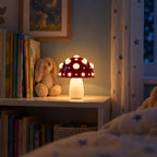 Small red mushroom lamp with white spots glowing as a night light on a child's bookshelf