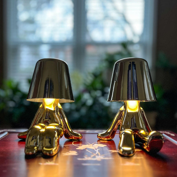 Two gold figure lamps glowing on a red table by a window