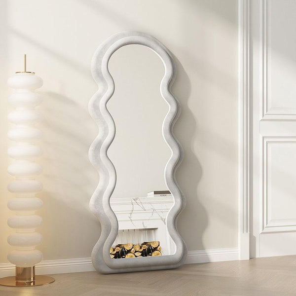 Light gray velvet wavy mirror beside a stacked globe lamp