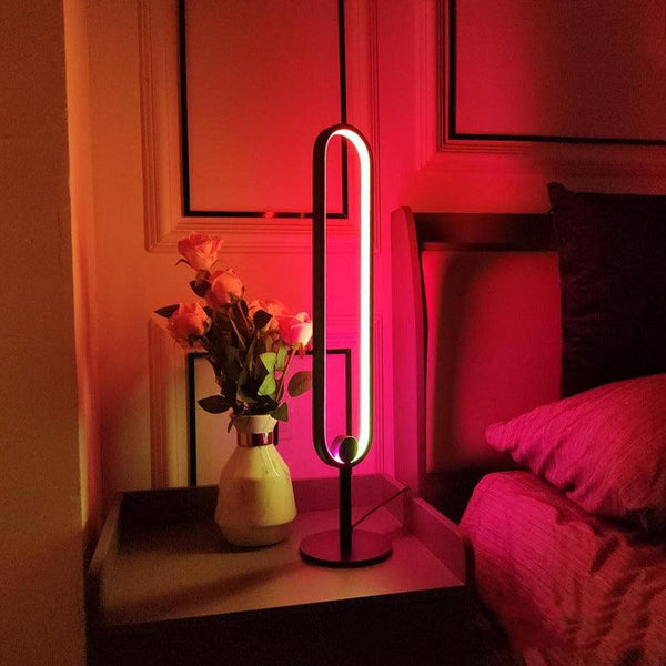 Black oval LED table lamp glowing red beside a vase of roses