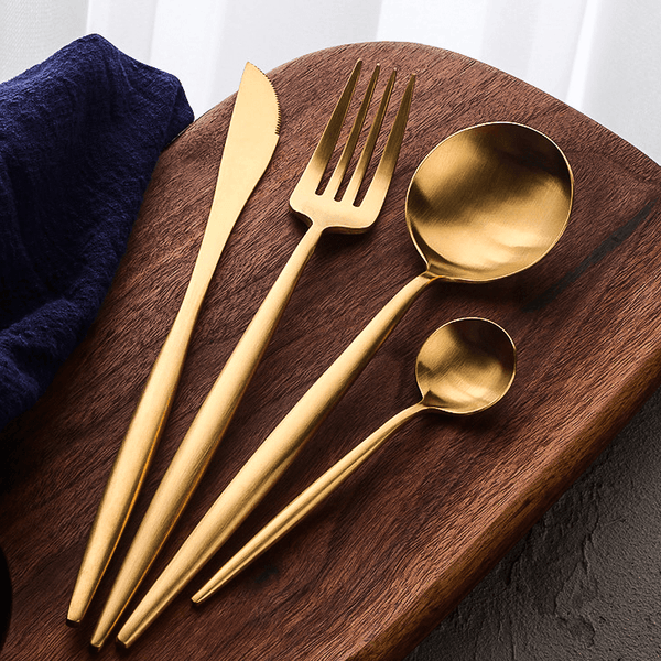 Gold flatware set laid on a wooden board with a navy napkin