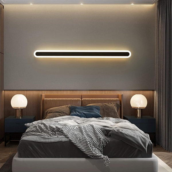 Black linear LED wall lamp mounted horizontally above a bed
