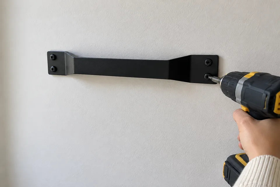 Close-up of the black wall bracket screwed flat to the wall, its raised middle leaving a slot for the hook